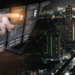 Businessman using futuristic digital interface for property management strategy and real estate data analytics with city nightscape. PropTech, smart investment, digital transformation.