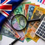 Australian flag next to various Australian dollar bills, a calculator, a pen, and a magnifying glass placed on financial charts, representing finance or economy in Australia.